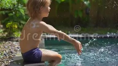 一个小男孩，肩膀上有一个<strong>防晒霜</strong>吸引的太阳，在游<strong>泳池</strong>里泼水。 太阳保护